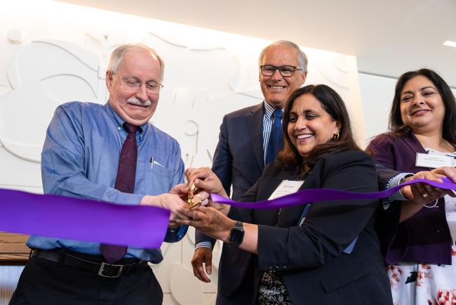 Onlookers smile as a man cuts a large purple ribbon with large scissors.