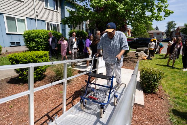 A man walks up an accessible ramp with a walker.