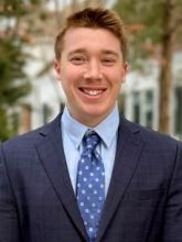 Photo of Rob, outdoors, wearing a blue suit, shirt, and patterned tie